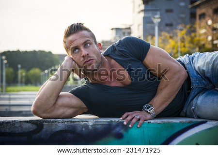 Handsome muscular blond man lying down in city setting looking to a side