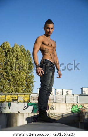 Full length shot of handsome fit athletic shirtless young man in city setting looking at camera