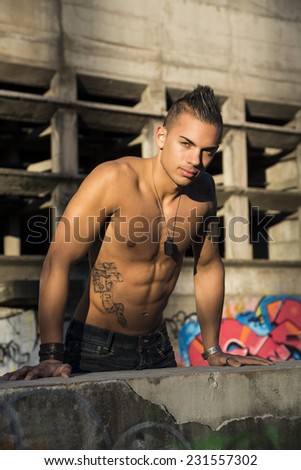 Handsome fit athletic shirtless young man in city setting balancing on concrete wall