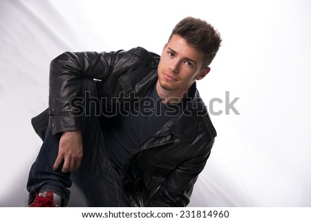Handsome young man or teenager sitting on white floor, wearing black leather jacket