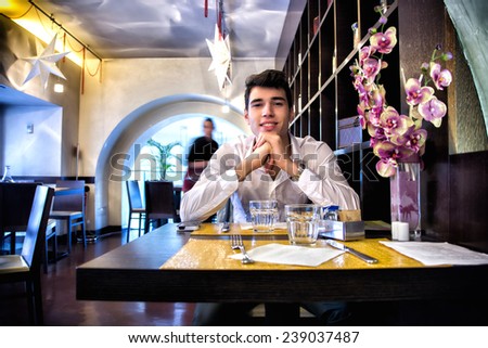 Handsome young man having lunch in elegant restaurant alone smiling and looking at camera
