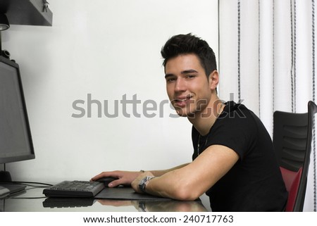Handsome young man working or studyiing at computer at home or in office, smiling at camera