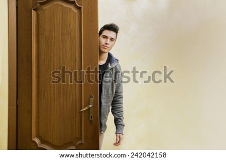 Handsome young man behind open door, getting out, looking at camera with friendly expression
