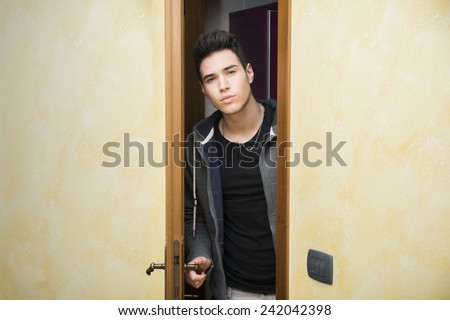 Handsome young man opening door to enter into a room, looking at camera
