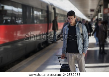 Handsome young male traveler in train station with trolley suitcase, looking down