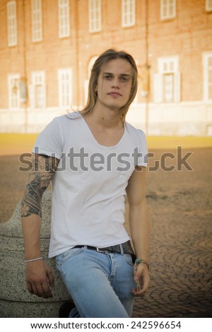 Handsome Long Hair Man on White Shirt Standing in Square in Turin city Center, Italy, with Old Palace Behind Him