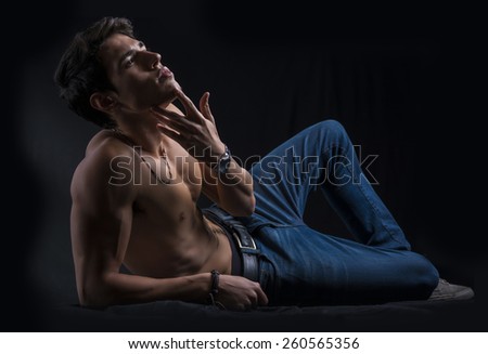 Handsome muscular shirtless young man laying down on the floor confident, profile view, looking up