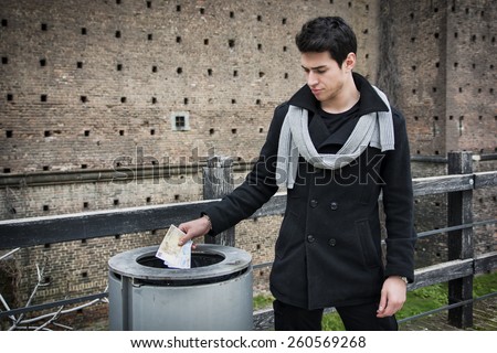 Handsome stylish young man standing outdoors throwing trash in a can as he protects the environment