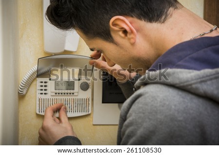 Over the shoulder close up view of a young man standing checking the speaker phone or intercom and alarm system at his apartment or house displaying the keypad and digital readout
