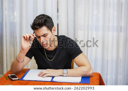 Handsome young man studying or doing homework or paperwork at home sitting at table