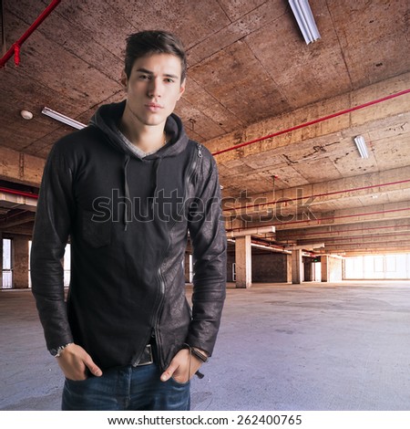 Trendy attractive young man standing in empty warehouse or industrial building, looking at camera