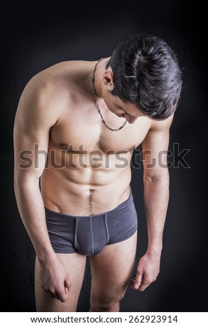 Handsome, fit young man wearing only underwear standing on black background, looking down