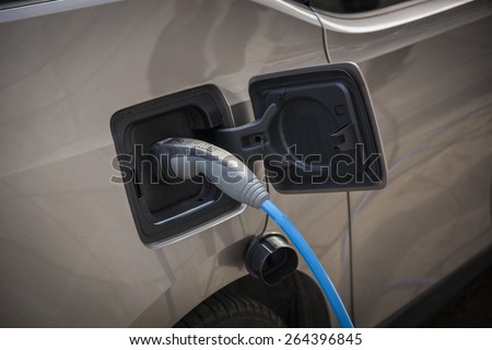 Charging an electric car at a roadside urban charging station showing a close up of the attached connector and cable in a green energy concept