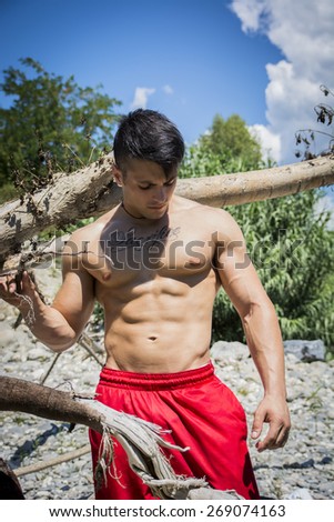 Attractive muscular shirtless young man in nature with plants, branches, river
