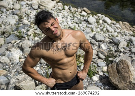 Attractive muscular shirtless young man in nature with plants, branches, river