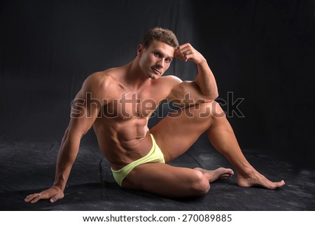 Attractive shirtless muscular man laying down on the floor in bathing suit on dark background