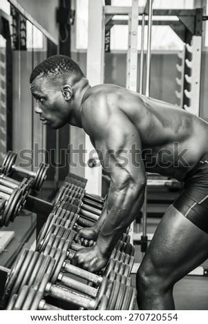 Handsome black male bodybuilder resting after workout in gym, leaning tired on weights