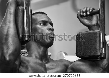 Hunky muscular black bodybuilder working out in gym, exercising pecs on machine