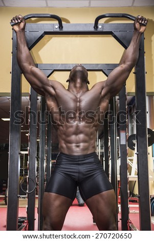 Hunky muscular black bodybuilder working out in gym, exercising back with dumbbells