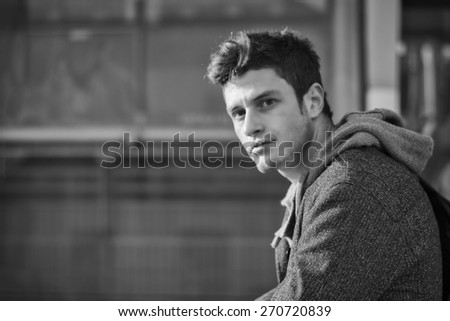 Handsome young man in city setting, lit by sunset light, looking at camera in a black and white shot