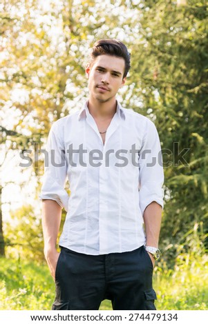 Attractive young man standing in a forest, looking at camera