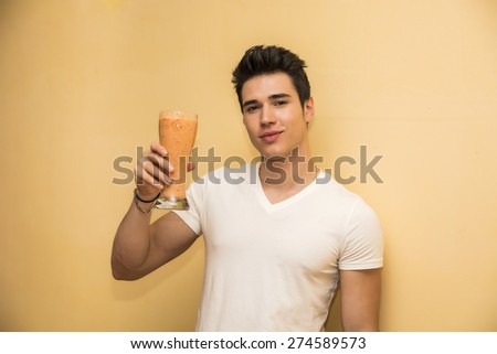 Young man saluting with a healthy smoothie drink made from blended fresh tropical fruit offering a toast or greeting