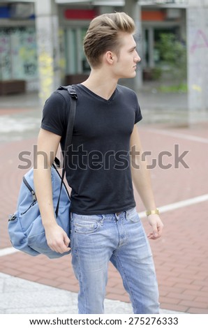 Attractive young man wearing black T-shirt and jeans with back pack standing outside