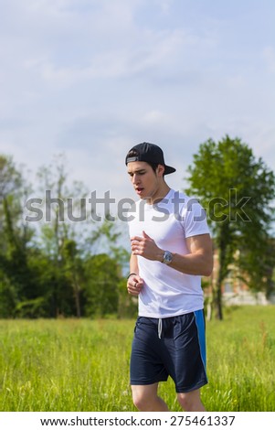 Handsome young man running and jogging on road in the country in a sunny day, wearing white shirt and baseball cap