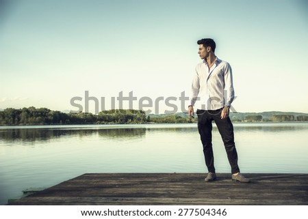 Handsome young man on a lake in a sunny, peaceful day,standing on a wood pier