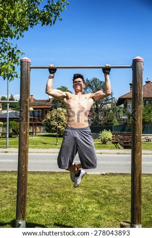 Attractive shirtless young man exercising and working out in outdoor gym in city park