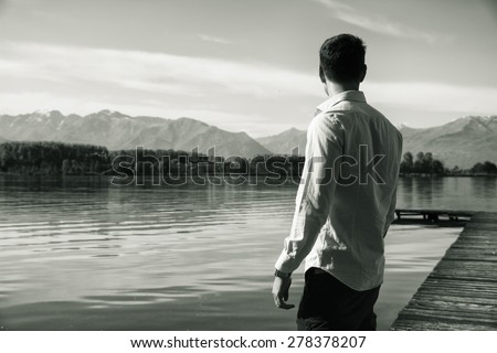 Handsome young man on a lake\'s shore in a sunny, peaceful day, standing. Black and white shot