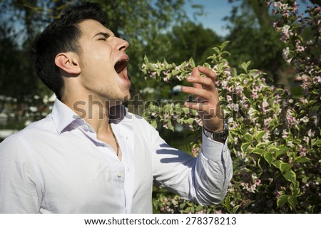 Attractive young man next to flowers sneezing because of hay-fever allergy