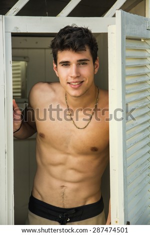 Waist Up Portrait of Handsome Shirtless Smiling Young Man Leaning Out of Cabana Door, Portrait of Male Surfer Standing in Doorway of Rustic Beach Hut
