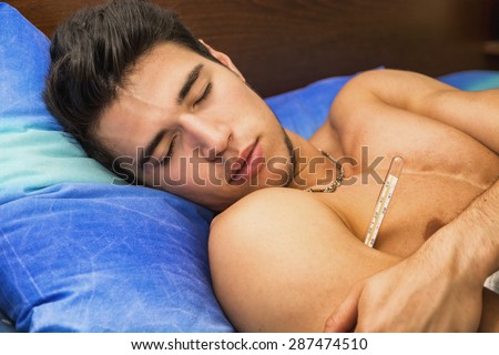 Young handsome man in bed with a flu or measuring fever with thermometer in his mouth