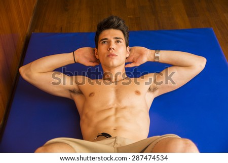 Attractive blond young man shirtless in gym working out, doing exercises for abs