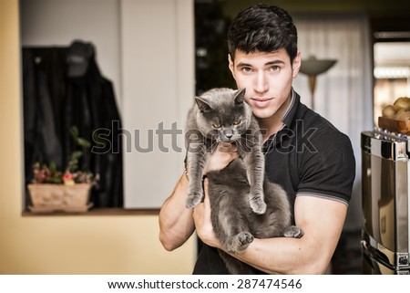 Handsome Young Animal-Lover Man Inside the House, Hugging his Gray Domestic Cat Pet.