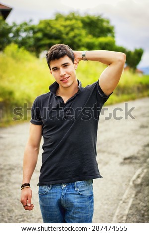 Sexy handsome young man in jeans and black t-shirt walking along rural road