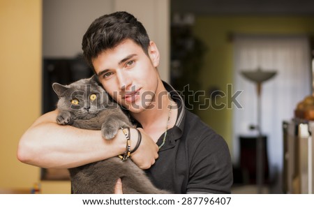Handsome Young Animal-Lover Man Inside the House, Hugging his Gray Domestic Cat Pet.