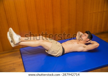 Attractive blond young man shirtless in gym working out, doing exercises for abs