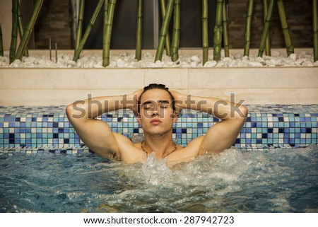 Young Man with Eyes Closed and Hands Behind Head Relaxing in Spa Whirl Pool in Tranquil Setting