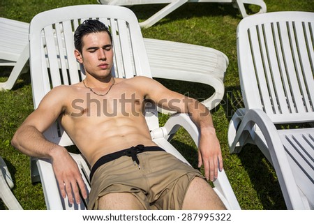 Shirtless Young Man Drying Off in Hot Sun, Muscular Man Wearing Bathing Suit and Sunglasses Sunbathing on Pool Side Lounge Chair on Grass