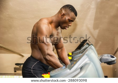 Hunky shirtless muscular black male bodybuilder exercising on step machine in gym