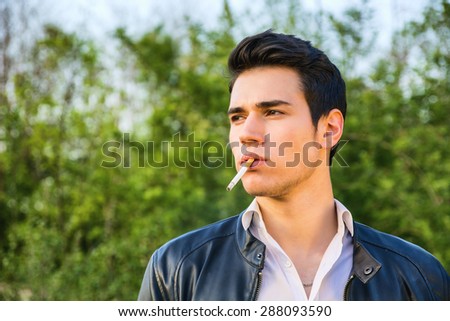 Handsome young man at countryside, in front of field or grassland, wearing white shirt and jacket, looking away to a side