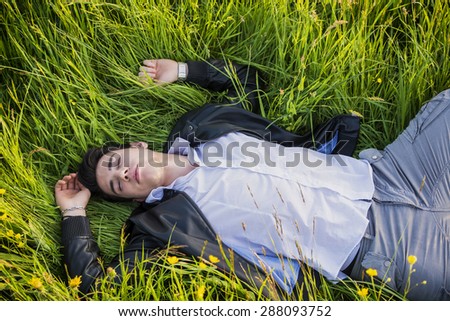 Good looking, fit male model relaxing lying on the grass, with eyes closed, photographed right from above