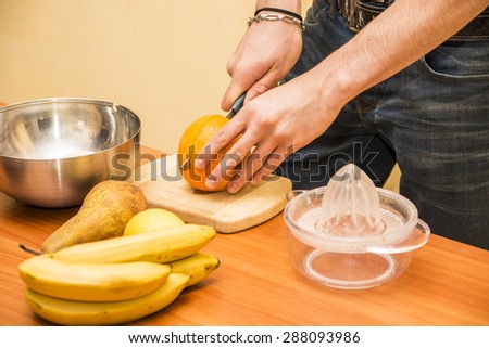Close-up of hands of a man preparing a healthy fruit salad or smoothie, standing leaning on a kitchen counter loaded with an assortment of fresh tropical fruit