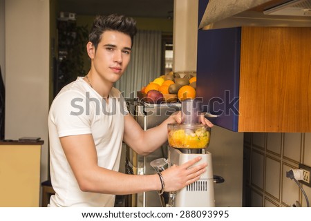 Young man preparing healthy smoothie drink in mixer, made from blended fresh tropical fruit offering a toast or greeting