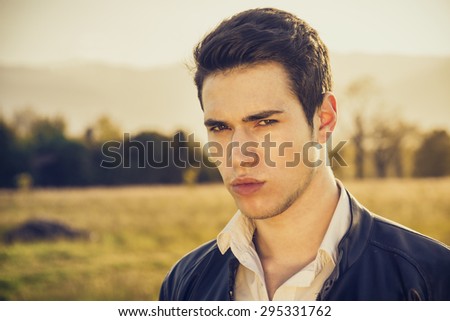 Handsome young man at countryside, in front of field or grassland, wearing white shirt and jacket, looking away to a side