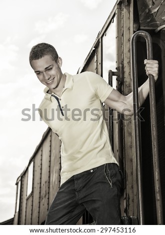 Fit guy with polo shirt hanging from old train, jumping dow while smiling