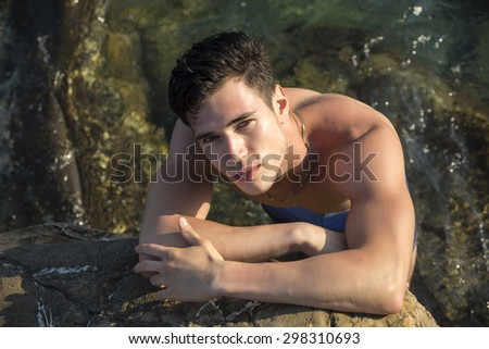 Muscular handsome young man at sea seen from above perspective, looking at camera