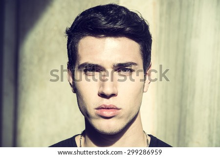 Handsome young man\'s headshot, looking intensely at camera with serious expression